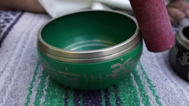 A green bowl with Chinese writing on it sits on a green and blue rug. The bowl is small and has a silver rim