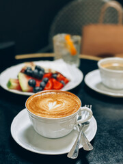 Delicious cappuccino with latte art on table in cafe with fruit plate and iced drink