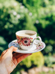 Woman holding floral teacup with green bokeh background
