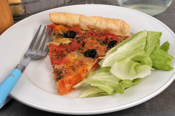 Assiette avec une tarte tomates mozzarella avec des olives noires et des feuilles de salade