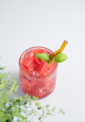 Glass of refreshing watermelon cocktail with basil and ice on a light background with fresh herb.