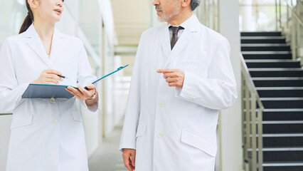 Fototapeta premium Man and woman in white coats consulting while walking in lobby