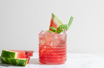 Glass of refreshing watermelon smoothie with basil, ice on white marble background with slice of...