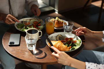 Couple having tasty breakfast at wooden table in cafe, closeup