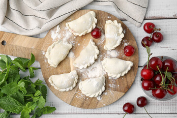 Raw dumplings (varenyky) and fresh cherries on white wooden table, flat lay