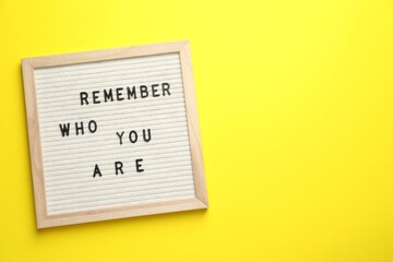 Letter board with phrase Remember Who You Are on yellow background, top view. Space for text