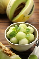 Melon balls in bowl and fresh fruit on wooden table, closeup