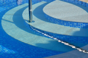 Swimming pool detail of tiles, steps and chrome handrail.