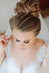 A woman with long brown hair and a white dress is wearing a white veil. She is wearing a pair of earrings and a necklace