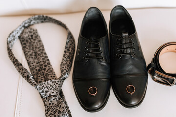 A black shoe with a ring on it sits next to a tie