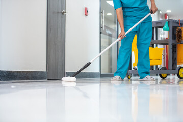 A mop operator in a blue uniform cleans new epoxy floor protection suits in an empty hospital...