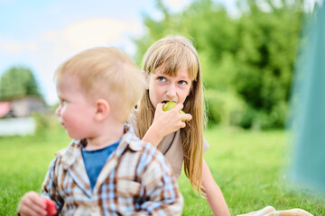 Happy Caucasian family on picnic sitting on blanket on green grass in backyard eating watermelon and having fun