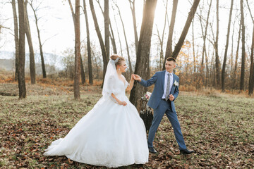 A bride and groom are walking through a forest, hand in hand. The bride is wearing a white dress and the groom is wearing a blue suit. Scene is romantic and peaceful