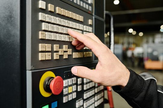 Close-up of a person's hand adjusting settings on an industrial control panel in a factory environment