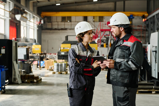 Two industrial workers wearing protective helmets and uniforms discussing work plans on a digital tablet