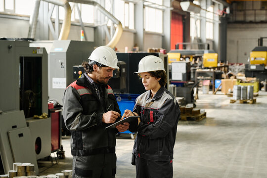 Workers in an industrial workshop engaging in discussion, dressed in protective work attire and helmets