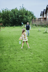 Fototapeta premium Teenage girl playing badminton with her father on green grass in summer park