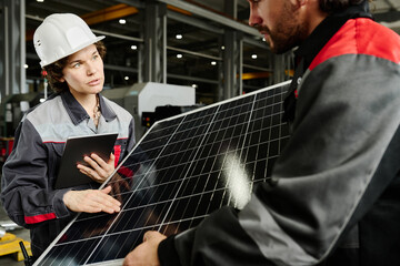 Workers examining solar panel in industrial setting wearing protective gear