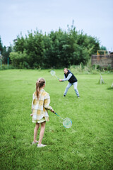 Fototapeta premium Teenage girl playing badminton with her father on green grass in summer park