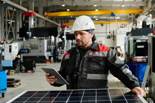 Engineer wearing a hard hat and work uniform examining solar panels. Industrial setting