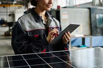 Technician examining solar panel in manufacturing workshop with serious expression