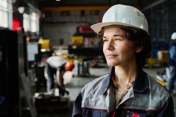 Focused female engineer inspecting industrial construction site while wearing safety gear and hard hat