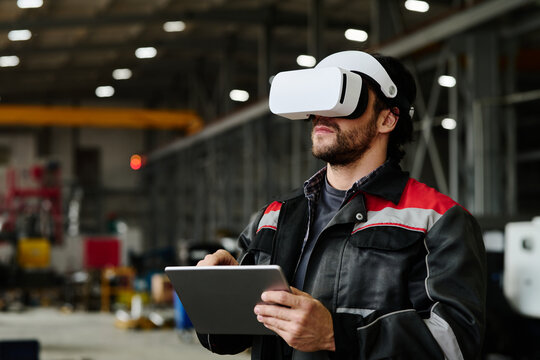 Individual in industrial environment experiencing virtual reality, while holding a tablet