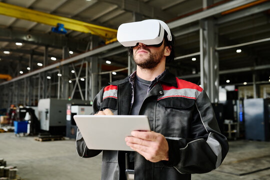 Adult male worker using virtual reality headset while holding digital tablet in hands