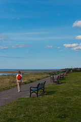 A woman strolls along a coastal path with benches overlooking the water