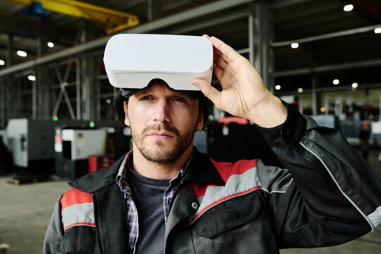 Man lifting side of virtual reality headset while standing in industrial factory setting