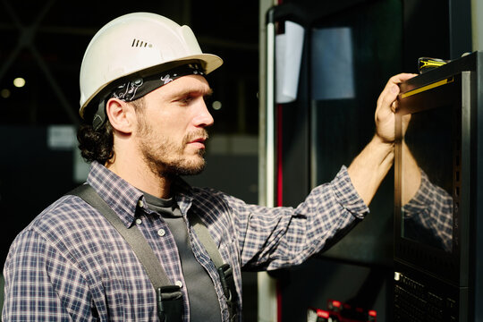 Bearded engineer in hard hat and plaid shirt operating machinery in modern industrial environment