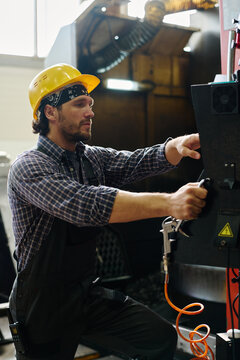 Worker wearing hard hat and bandana, operating heavy machinery in factory setting