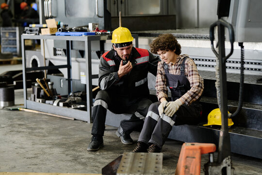 Two workers sitting on break in industrial workshop, discussing tasks and strategies