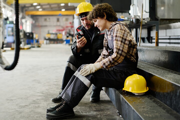 Two workers in protective gear huddling over instruction in industrial setting