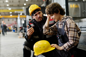 Two workers in workshop wearing hard hats engaging in conversation. Focus on person receiving guidance