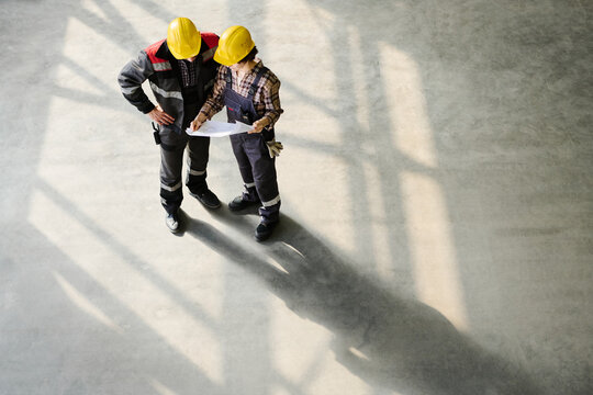 Construction workers standing on site reviewing blueprints and discussing project details in sunlight shadows - Powered by Adobe