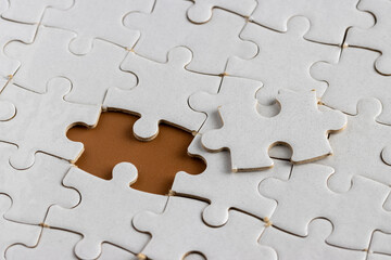 unfinished or incomplete white jigsaw puzzle on chocolate brown background. Last piece of puzzle. Business concept.