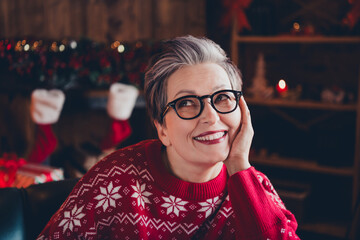 Photo of dreamy thoughtful woman wear red print xmas sweater glasses enjoying christmas arm cheek indoors apartment room