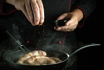 Sausage frying in a frying pan for dinner. The chef sprinkles aromatic dry spices on the meat sausage with his hands.