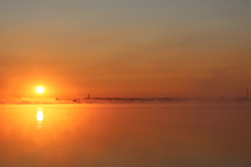 photo of a bright sunrise on a lake with haze