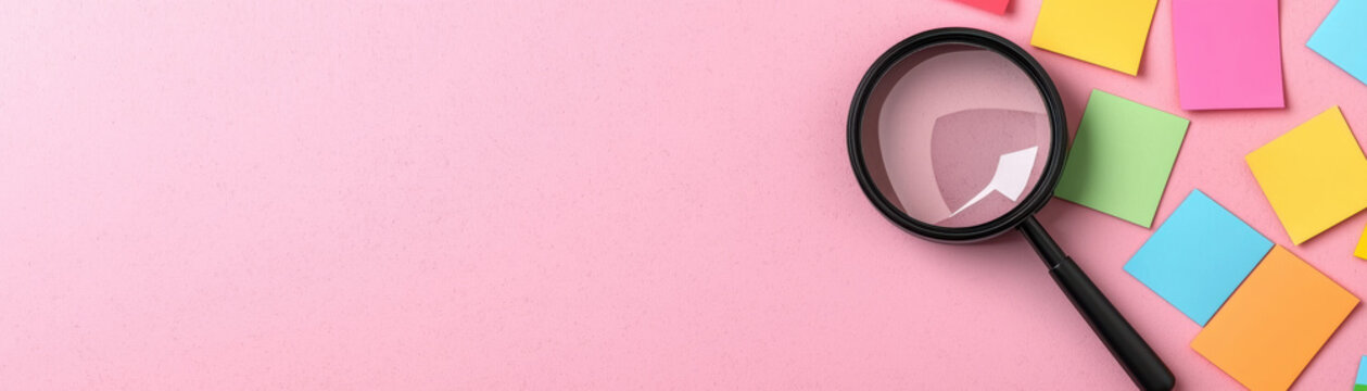 Magnifying glass and colorful sticky notes on a pink background. Concept for search, discovery, analysis, and organization.