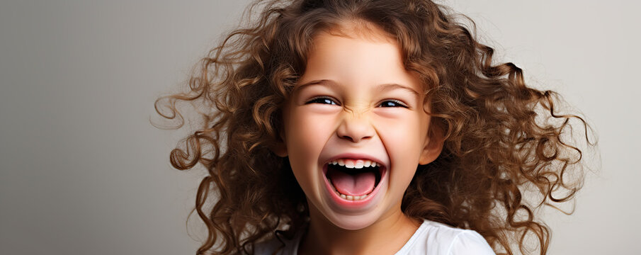 Joyful young girl with curly hair laughing against a light background, capturing the essence of childhood happiness and exuberance