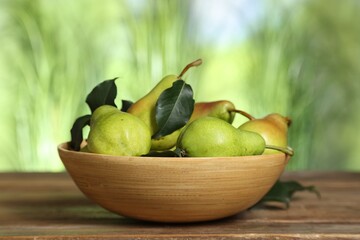 Fresh pears and leaves in bowl on wooden table against blurred green background, closeup