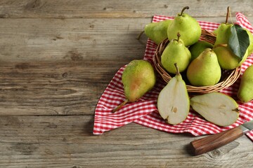 Fresh green pears, wicker basket and napkin on wooden table. Space for text