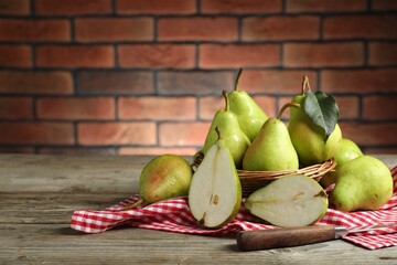 Fresh green pears and knife on wooden table against brick wall. Space for text