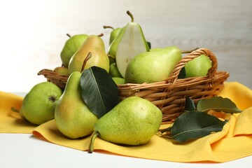 Fresh green pears with leaves and basket on white table, closeup