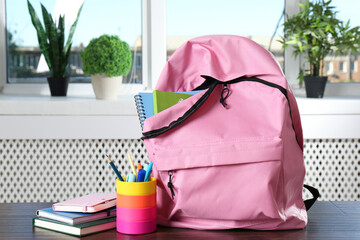 Backpack with different school stationery on wooden table indoors