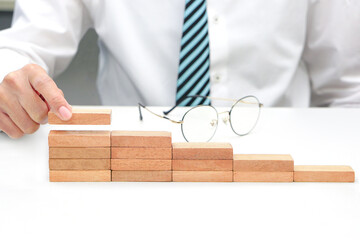 Hand holding a wooden block cube brought on as a stair step and blur glasses behind. Business strategy and target of business.