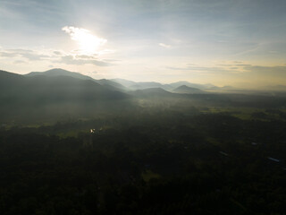 Aerial view of hills, green fields and forest while the sun rises in the back of the hills, it was shot in the sourrondings of Chiang Mai, in the Chiang Mai province of northern Thailand
