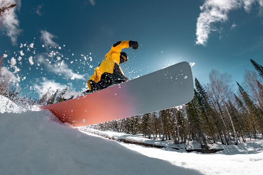 Professional young snowboarder jumps from the kicker at the forest slope. Winter ski holidays resort concept